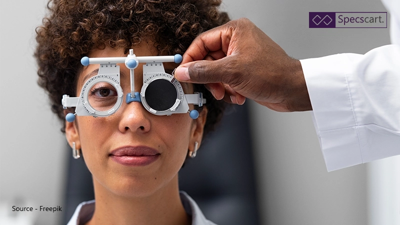 A woman having an eye examination using a phoropter to determine her correct prescription, symbolising the need for workplace eye tests and glasses funding.