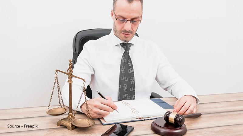 A professional wearing glasses sits at a desk, writing in a notebook next to a gavel and scales of justice, symbolising the legal right to claim eye care costs.
