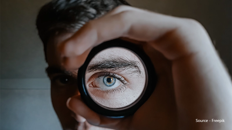 A dramatic close-up of a blue eye, viewed through a circular lens or opening, emphasises the structure of the iris, pupil, and surrounding eye area.