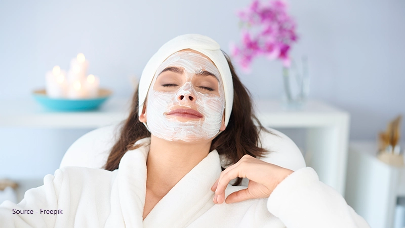 Woman in a white robe with a facial mask, highlighting skin care and hygiene to prevent irritation from glasses.