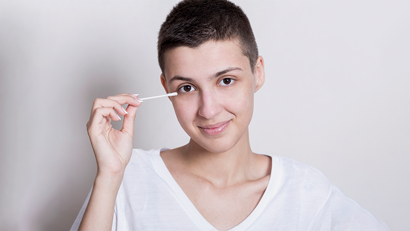 A woman with short hair using a cotton swab near her eye, demonstrating a precise way to remove eye makeup naturally.