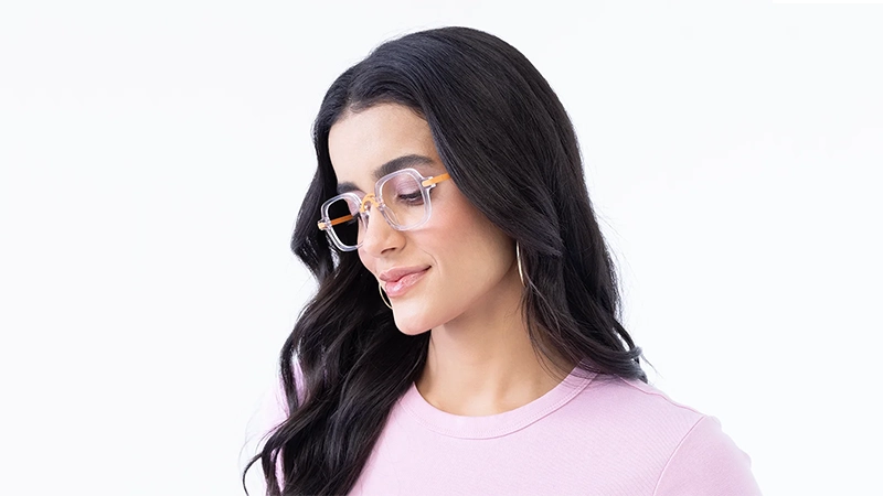 Woman wearing transparent geometric glasses with orange arms and a sculptural raised bridge.