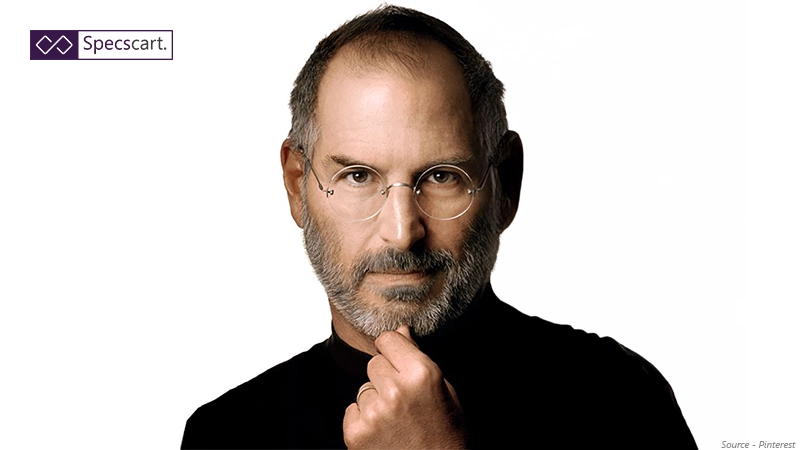 Iconic portrait of Steve Jobs wearing his signature round rimless glasses and black turtleneck, posing with his hand on his chin.