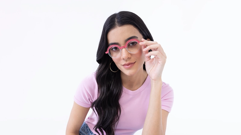 Woman with long dark hair wearing pink geometric round glasses, showing how bright frames contrast with dark hair colours.