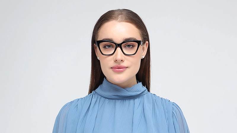 Woman in a blue blouse wearing bold black cat-eye glasses, conveying a sense of authority, elegance, and sophistication.
