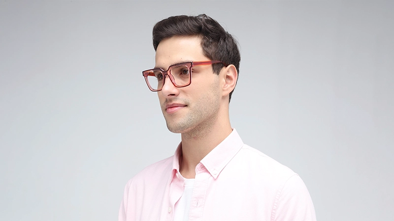 A man wearing bold red square glasses and a pink shirt, illustrating a warm and confident fashion choice.