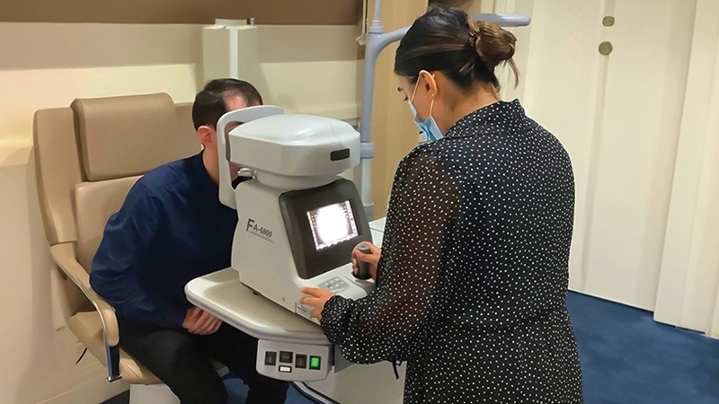 Optometrist using a white autorefractor machine to test a patient's eyes during a clinical eye exam.