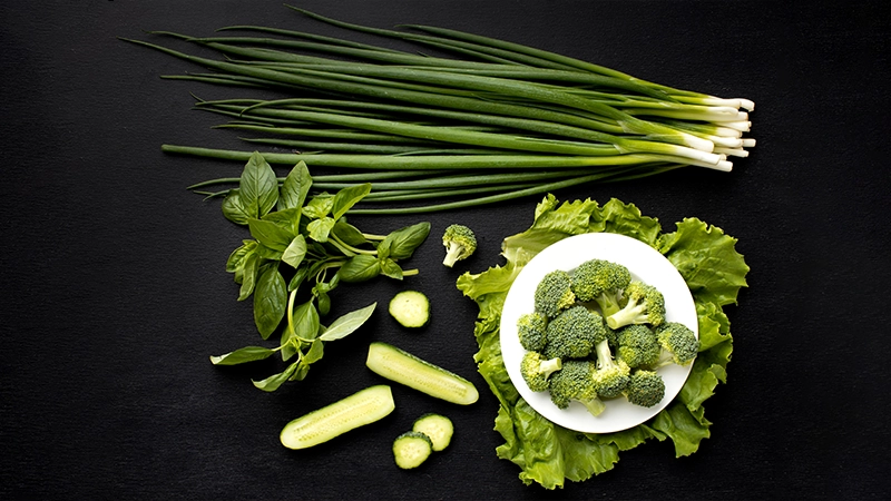 Fresh green vegetables, including broccoli, cucumber, and scallions, represent nutrient-rich foods for healthy eyes.