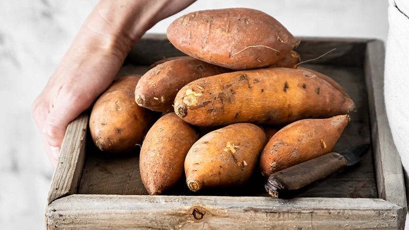 A wooden crate filled with sweet potatoes, highlighting beta-carotene-rich food for healthy eyes.
