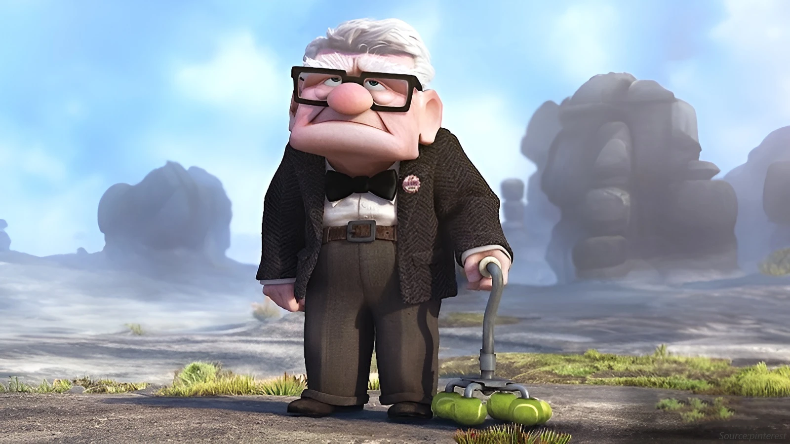 The CGI character Carl Fredricksen from Up stands outdoors, leaning on a walker with tennis balls. He wears a suit jacket, bow tie, and his signature thick, black square glasses.