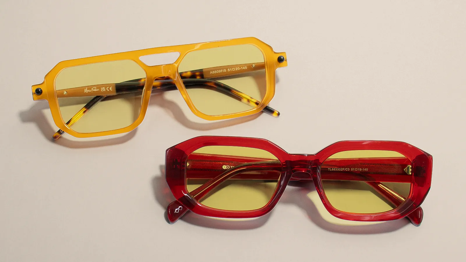There are two pairs of bold, stylish sunglasses with tinted yellow lenses. One has a bright yellow geometric frame, while the other has a striking red angular frame, both designed to combine fashion with eye protection.