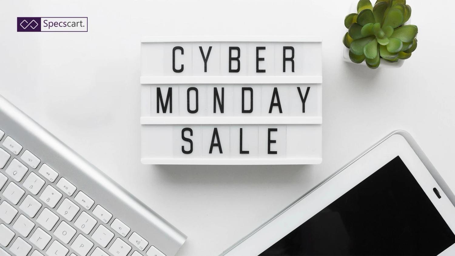 Lightbox with the words “Cyber Monday Sale” placed on a white desk with a keyboard, tablet, and small green plant.