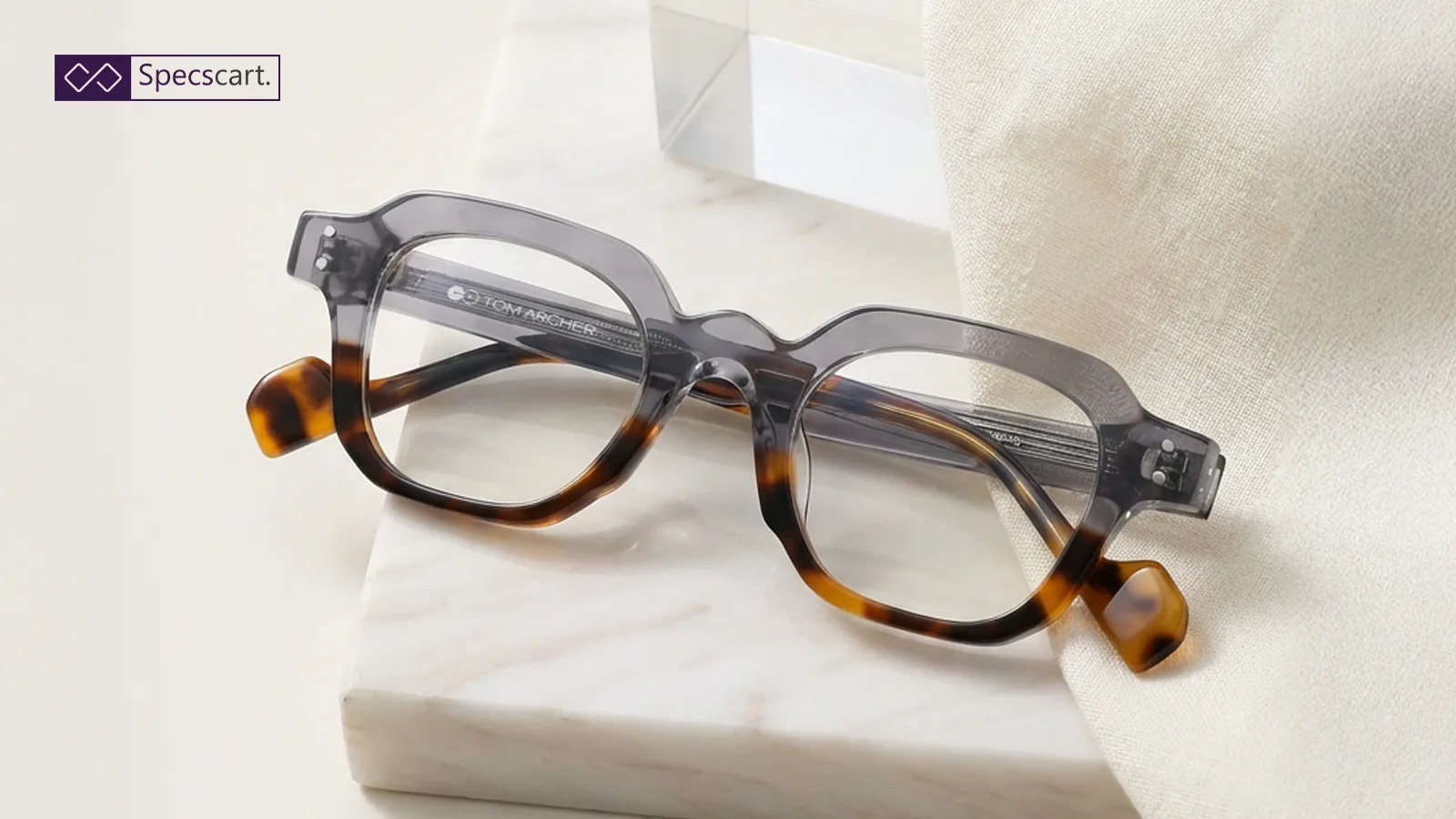Stylish Tom Archer glasses with a grey and tortoiseshell frame resting on a marble slab, showcasing clear plano lenses for a fashion-forward look.