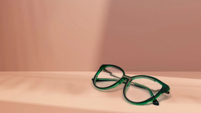 A pair of trendy green-framed glasses resting on a soft pink surface, showcasing a modern eyewear design suitable for multi-focal or varifocal lenses.