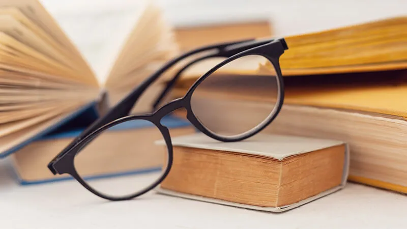 Stylish black round-framed glasses resting on a stack of books, representing the essential role of reading glasses for book lovers and students.