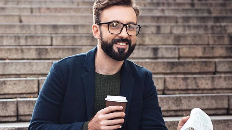 Man with a well-groomed beard wearing classic black rectangular frames, illustrating eyewear for professional beard styles.