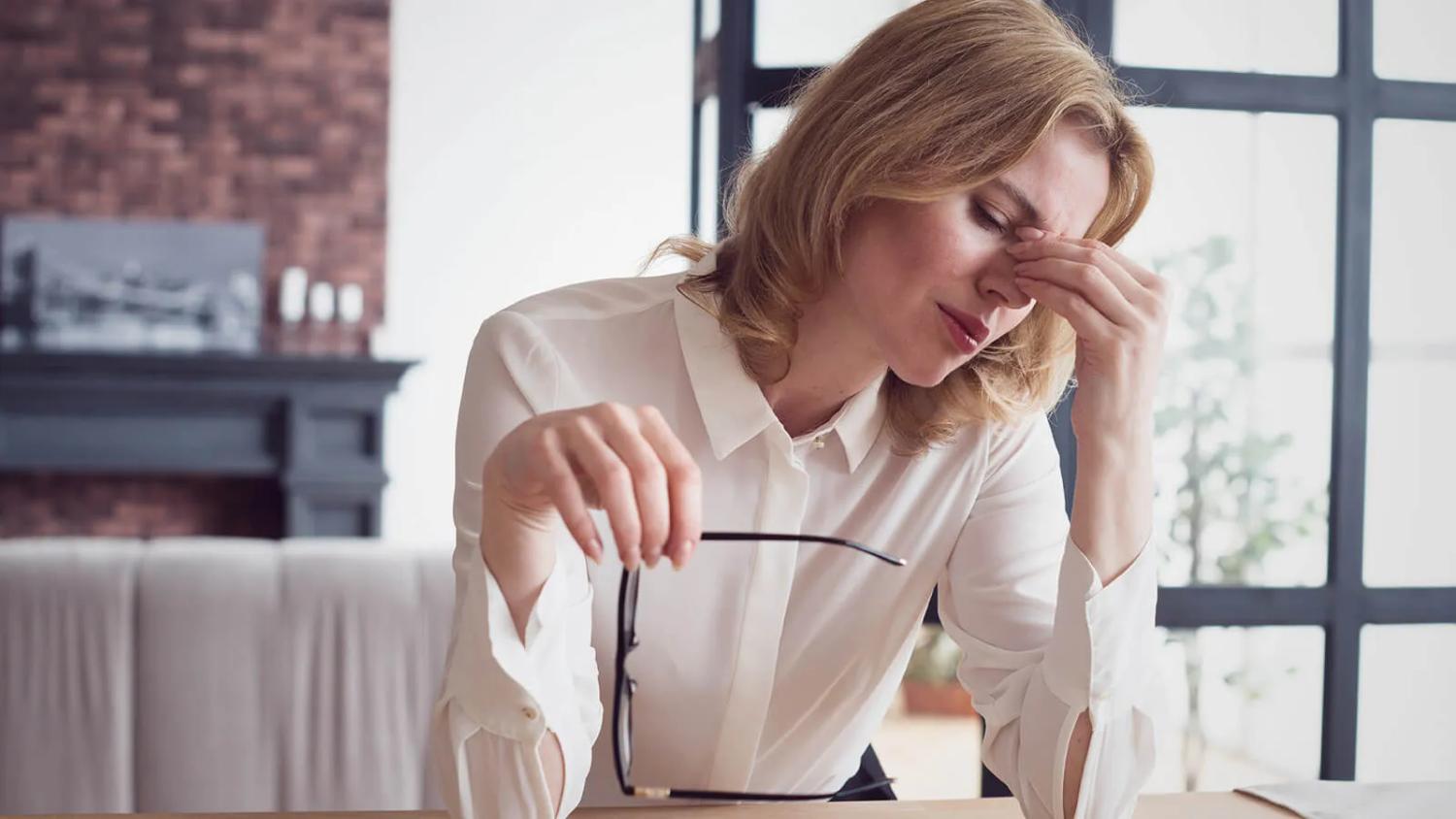 Stressed woman experiencing eye discomfort and twitching symptoms while working at a desk.