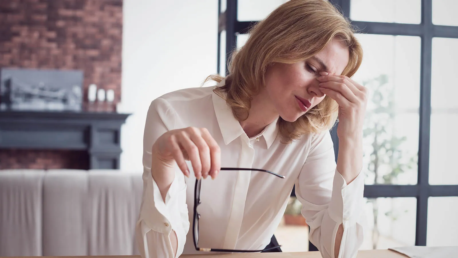 Stressed woman experiencing eye discomfort and twitching symptoms while working at a desk.