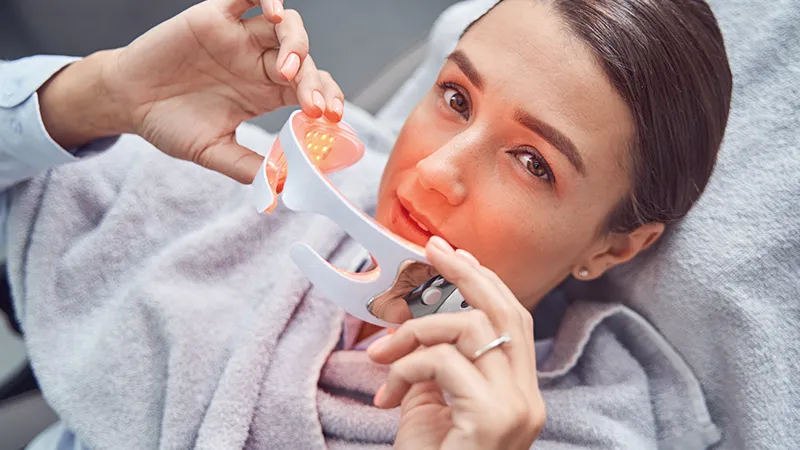 Woman lying down holding white light therapy glasses with glowing orange lights inside.
