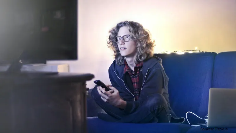 How to Choose the Perfect Frame Size for Varifocal Lenses A woman wearing glasses watches TV in a dark room, highlighting how properly sized varifocal frames ensure comfortable vision for daily activities.