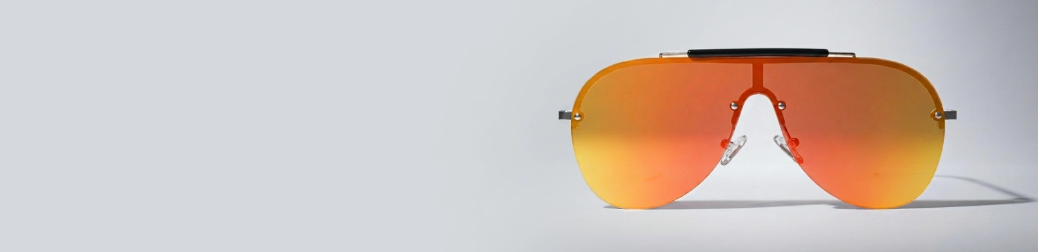 Oversized square sunglasses with silver mirrored lenses and a black and white speckled frame, resting on a white geometric block.
