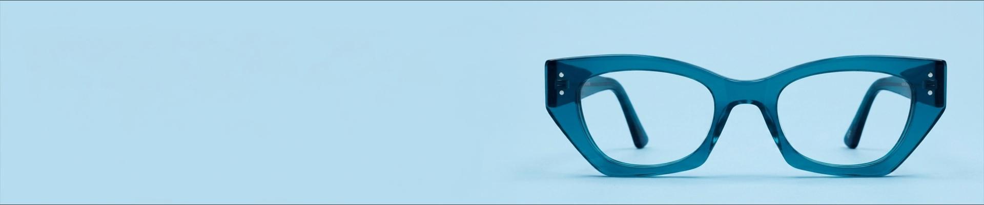 Blue Glasses Glossy round blue eyeglasses with keyhole bridge, placed upright on a white marble surface with matching marble background