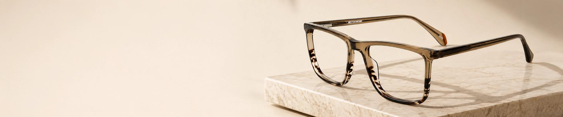 Brown Glasses Image featuring a pair of modern, thick-rimmed brown tortoiseshell glasses with clear lenses, showcasing their reflection on a light, smooth surface, featuring brown glasses page.