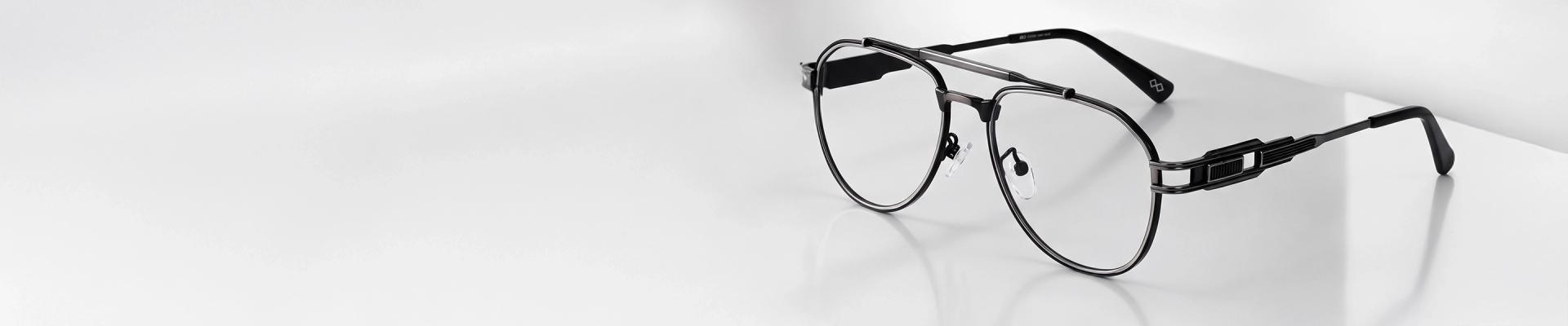 Gunmetal Glasses Classic round glasses with thin, minimalist gunmetal-colored metal frames resting on a light, curved surface.