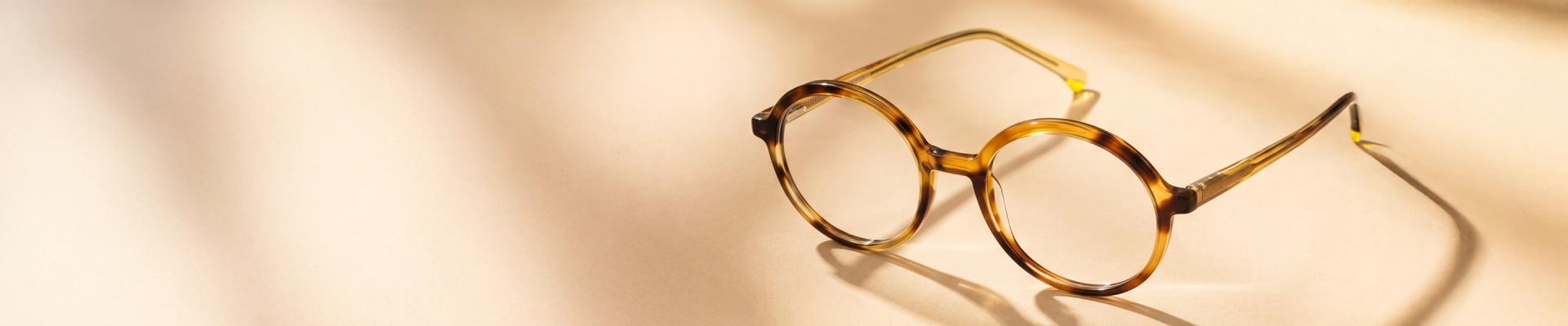 Yellow Glasses A smiling woman wearing stylish, oversized yellow and black round glasses looks up and to the side against a pale yellow background.