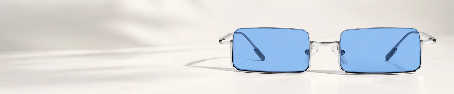 Silver Sunglasses A pair of lightweight silver sunglasses with blue-tinted lenses, displayed at an angle to highlight the sleek metal frame and minimalist design.