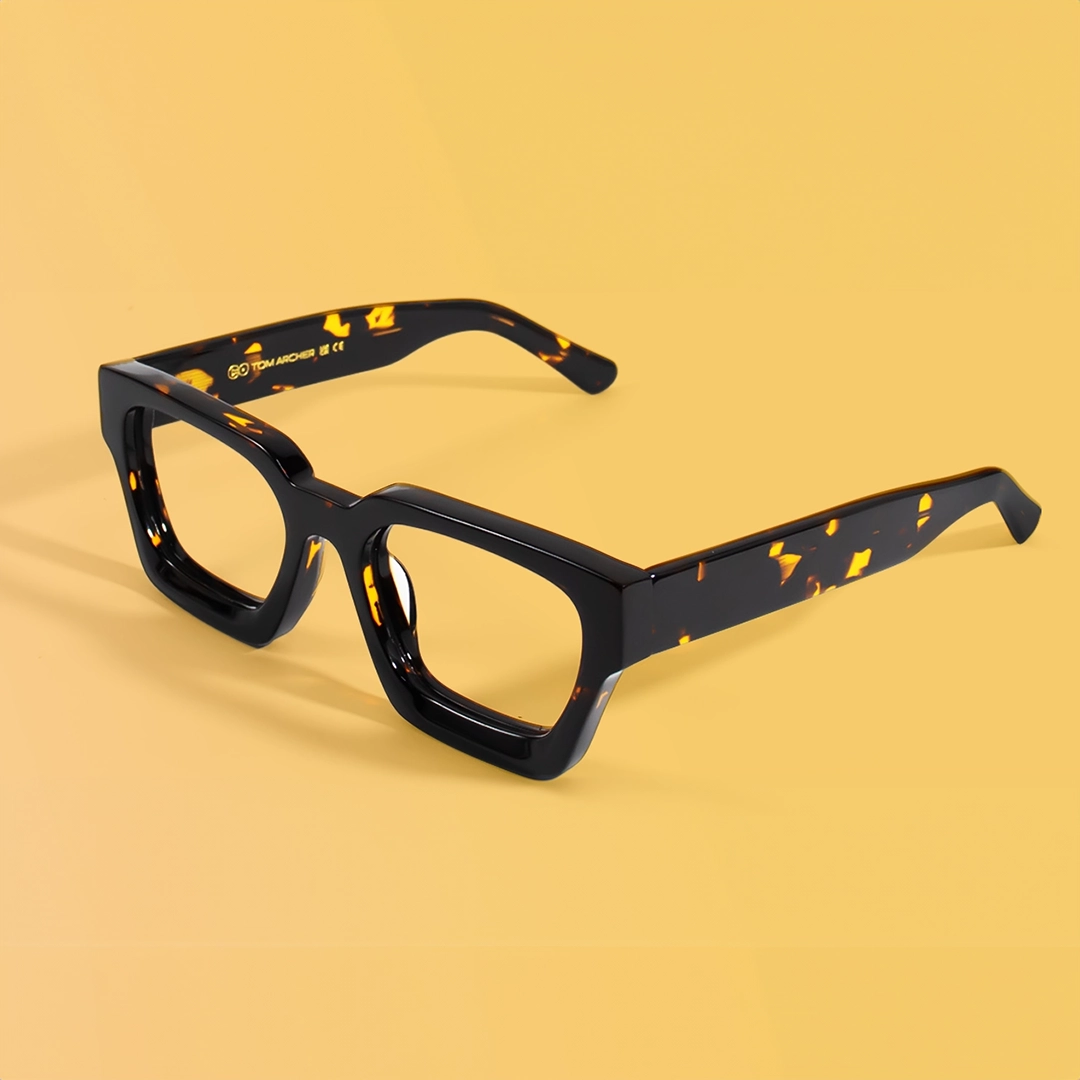 Thick-rimmed rectangular glasses in glossy black acetate with bold yellow tortoiseshell accents, displayed against a solid pale yellow background. The glasses have clear, non-prescription lenses, showcased as fashionable fake glasses for style without vision correction.