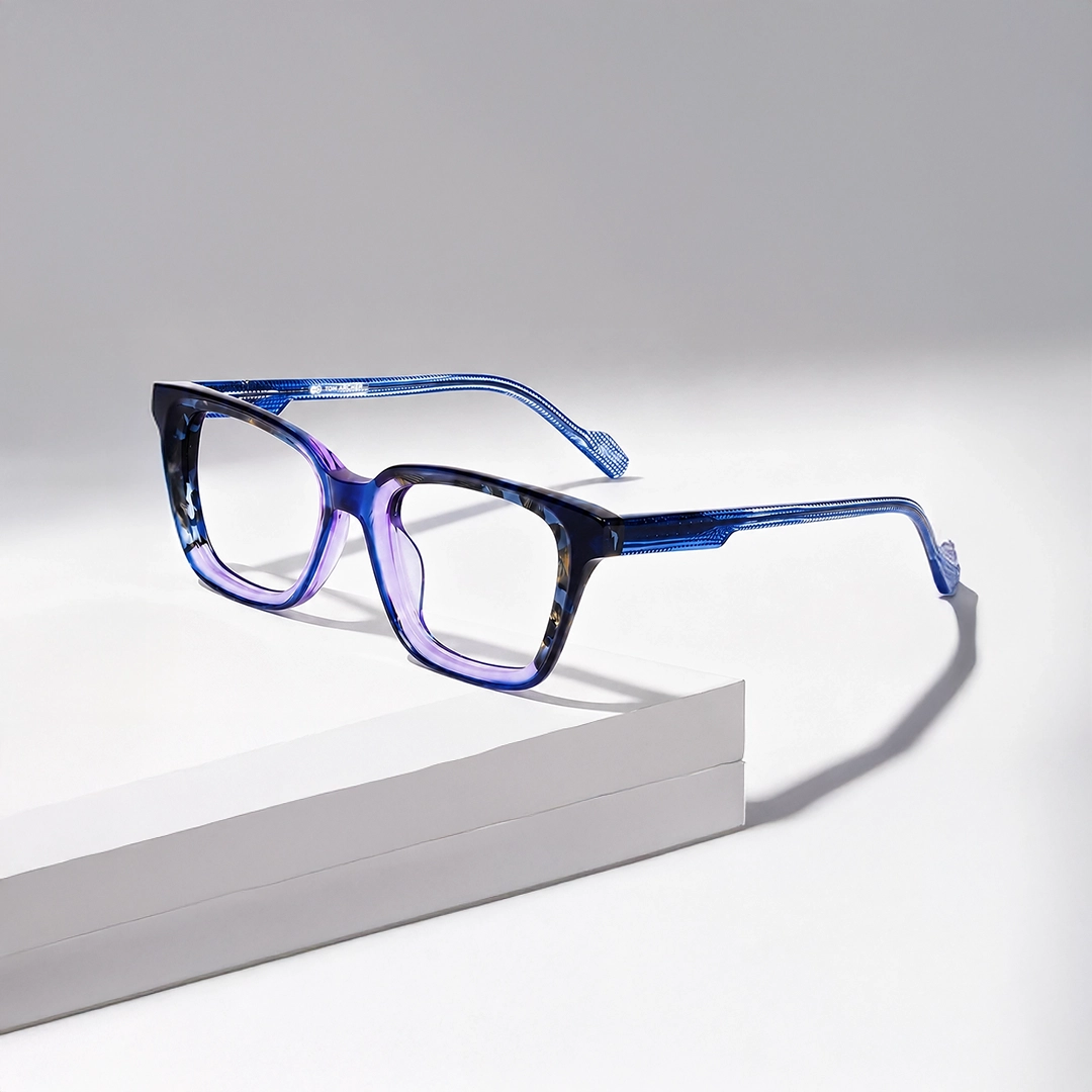 Purple Glasses Image showing a sleek pair of purple cat-eye prescription glasses with thin silver metal detailing on the sides, resting on a white cylindrical display stand, advertising purple glasses.