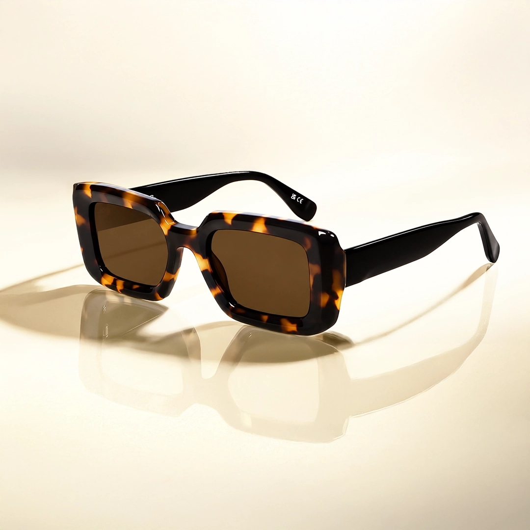Tortoise Shell Sunglasses Smiling woman with hair tied back wearing chic rectangular tortoiseshell sunglasses with dark lenses, against a soft light blue gradient backdrop.