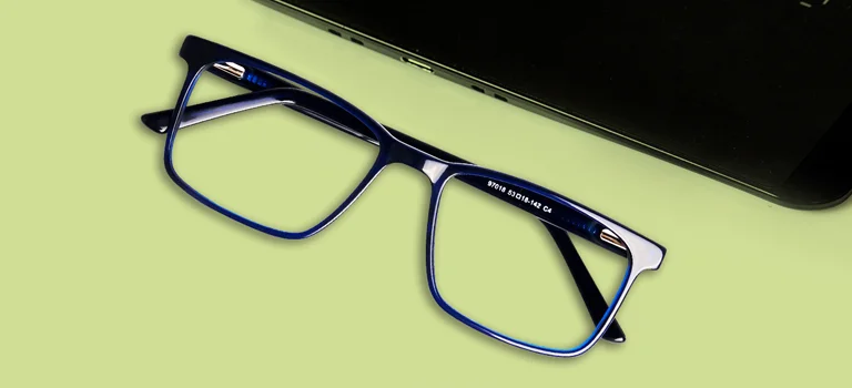 Blue rectangular glasses frames placed on a lime green desk next to a laptop, showcasing stylish and affordable eyewear for daily work.