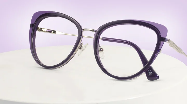 Image showing a sleek pair of purple cat-eye prescription glasses with thin silver metal detailing on the sides, resting on a white cylindrical display stand, advertising purple glasses.