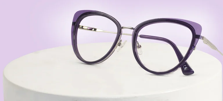 Image showing a sleek pair of purple cat-eye prescription glasses with thin silver metal detailing on the sides, resting on a white cylindrical display stand, advertising purple glasses.