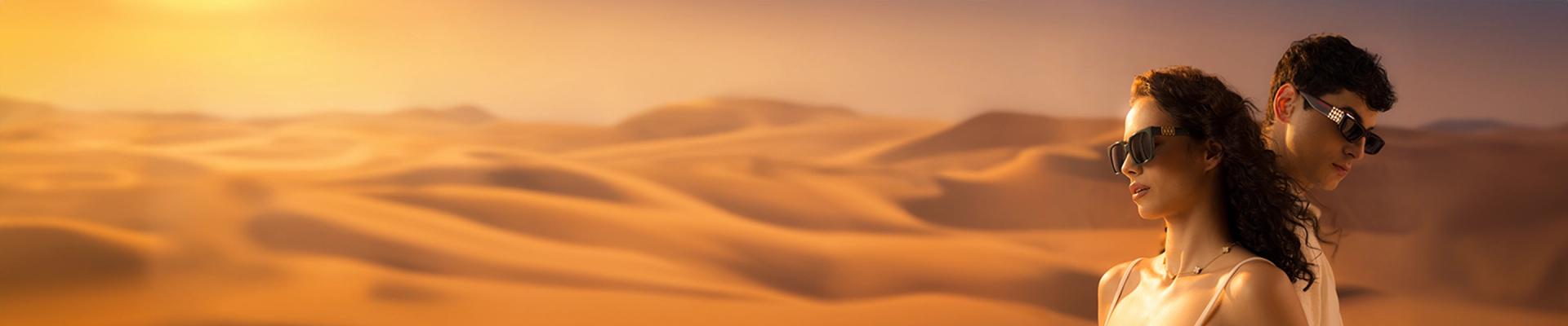 A man and woman pose back-to-back wearing premium designer sunglasses with gold temple details, set against a vast, golden desert dune landscape.