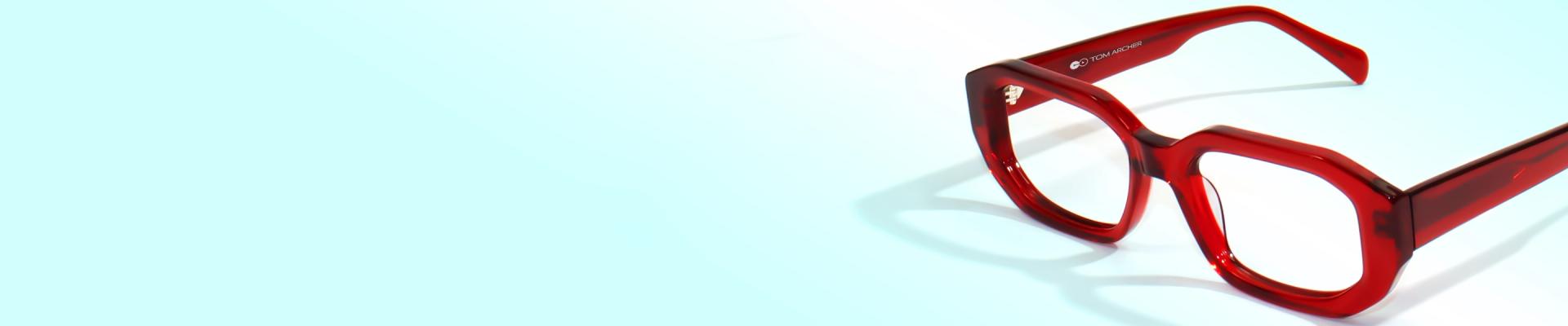 Close-up of stylish, bold, square glasses with bright, translucent red frames on a light blue background.