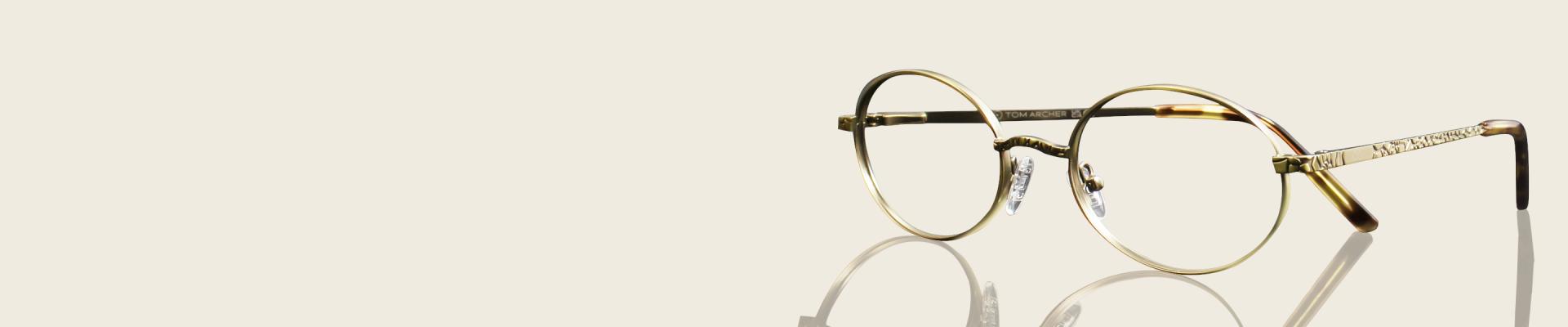 Elegant, vintage-style round glasses with thin, antique gold metal frames and tortoiseshell accents on the temples.