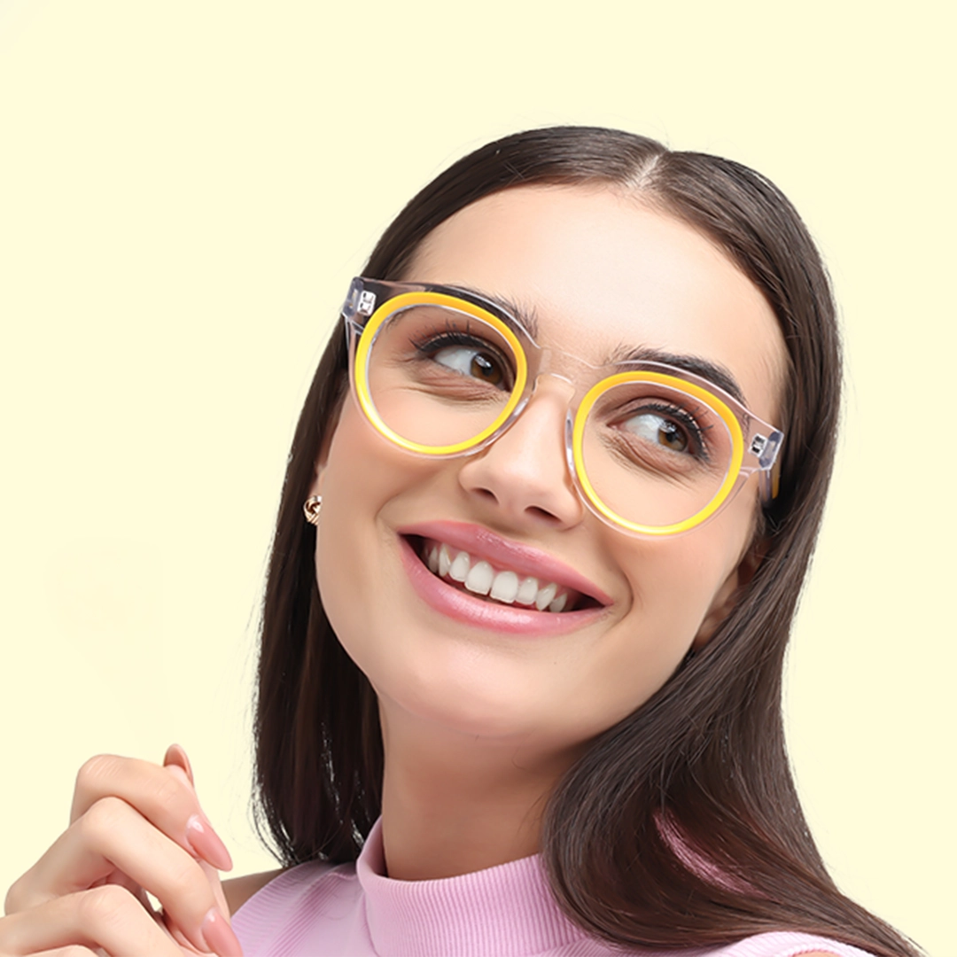 A smiling woman wearing stylish, oversized yellow and black round glasses looks up and to the side against a pale yellow background.
