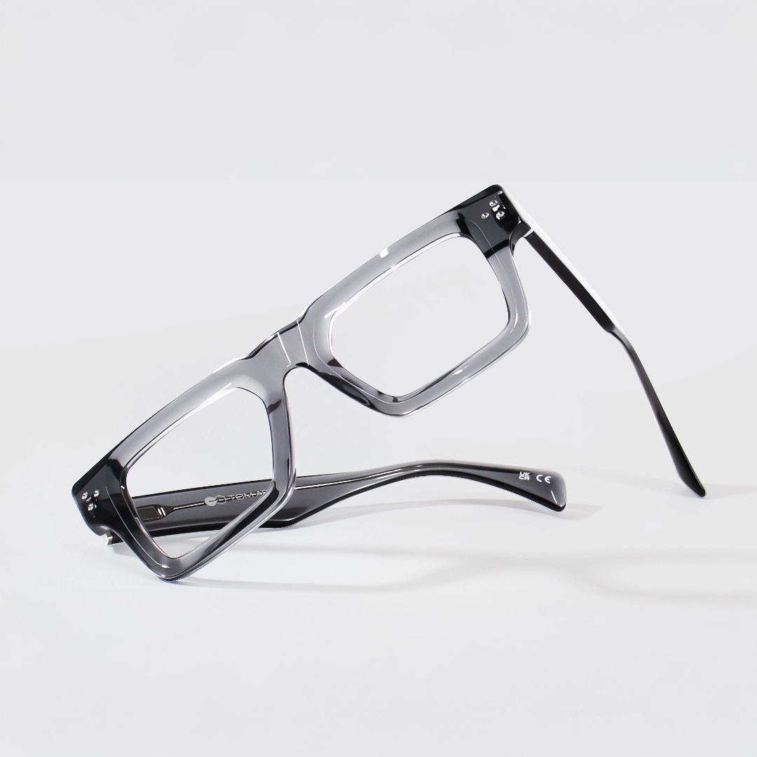 Stylish, angular square-framed glasses with glossy translucent grey frames, resting on a bright white background.