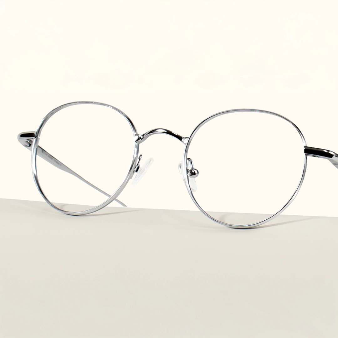 Gunmetal Glasses Classic round glasses with thin, minimalist gunmetal-colored metal frames resting on a light, curved surface.