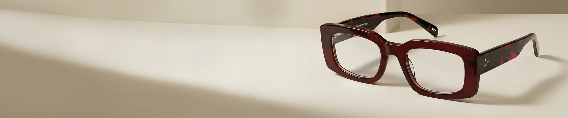 Rectangular Glasses Glossy rectangular glasses with thick black acetate frames accented by yellow and amber tortoiseshell patterns, shown on a pale blue background. The glasses have a modern, bold silhouette and feature subtle metallic detailing near the hinges.