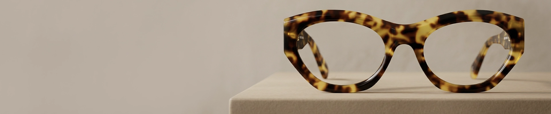 A close-up of stylish, angular tortoiseshell glasses with thick, bold frames, set against a light blue and white background.