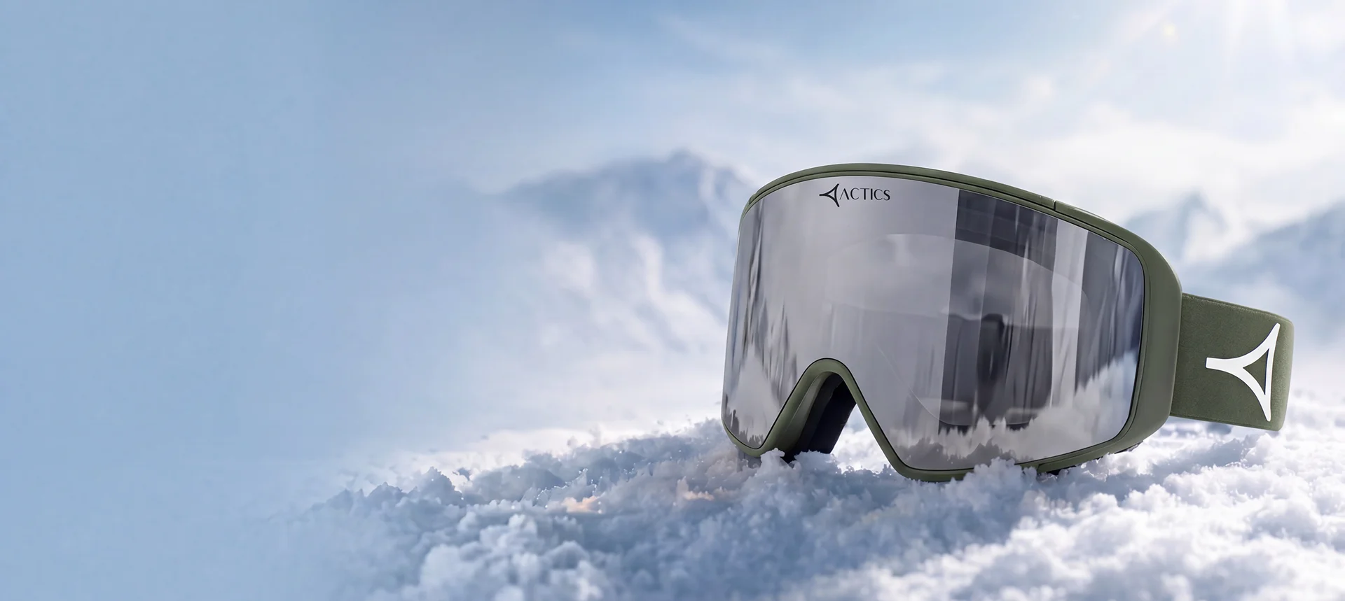 Ski goggles with a large, mirrored lens in icy blue, reflecting a dramatic snow-covered mountain landscape and cloudy sky. The goggles feature a sleek white frame and matching strap, prominently displaying the Specscart Actics logo in bold black. Placed in the foreground on pristine snow, the goggles stand out for their modern design and winter sports appeal, emphasising clarity, style, and adventure in a high-altitude setting.