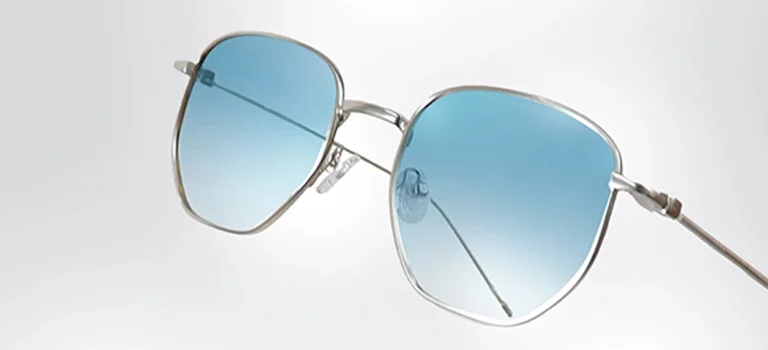Silver Sunglasses A pair of lightweight silver sunglasses with blue-tinted lenses, displayed at an angle to highlight the sleek metal frame and minimalist design.