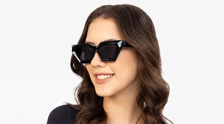 Geometric Sunglasses A woman with wavy brown hair wears thick black geometric sunglasses while smiling, set against a modern split background of light blue and white.