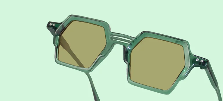 A close-up of premium black-framed pilots with polarised lenses, displayed on a geometric white block against a soft, bright background.