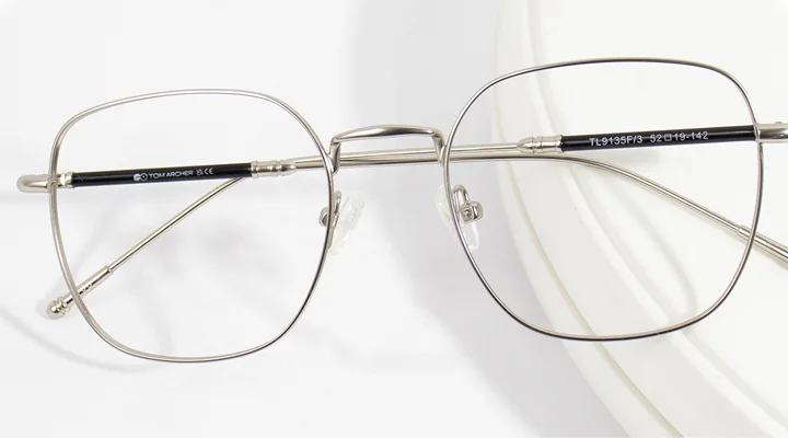 Lightweight silver titanium glasses with thin geometric frames resting on a clean white background, showcasing a durable and minimalist design.