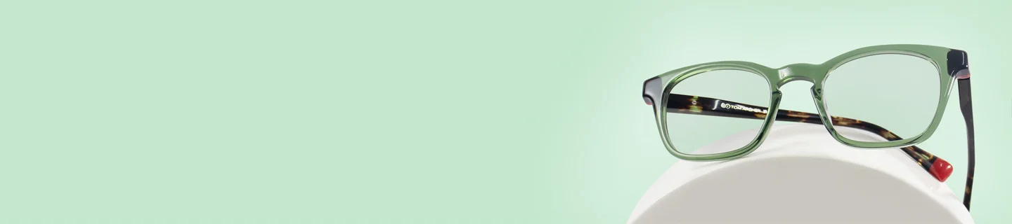 Green Glasses The image features a pair of green eyeglasses with black and tortoiseshell temples. It has a rectangular shape and is placed over a white stand against a light green background. It also has text saying Green Glasses, discount offer and Trustpilot Reviews.